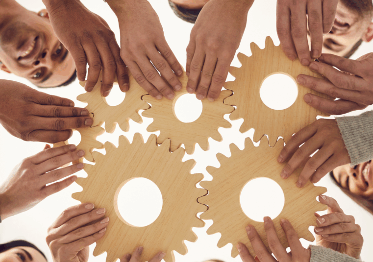 mitarbeitende halten fröhlich Holzräder ineinander was für Teamgeist und Zusammenarbeit im Change Prozess der SAP S/4HANA Transformation steht